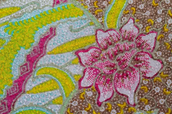 Yakın plan çekimde canlı bir batik kumaş görünür. Pembe, sarı ve mavi desenli karışık çiçek desenleri sergilenir..