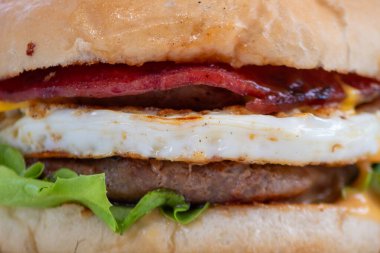 Yağda yumurta, domuz pastırması ve kıvırcık salatalı ağız sulandıran bir hamburgerin yakın çekimi..