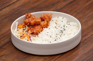 Kırsal bir masada beyaz bir kasede susamlı tavuk ve pilav.