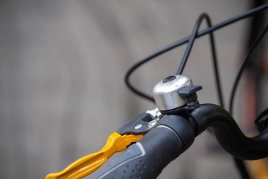 Gümüş zilli bisiklet gidonunun yakın çekimi, sarı fren kolu, ve siyah kablolar bulanık arka planda.