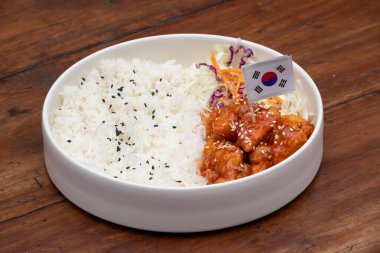 Kırsal bir masada beyaz bir kasede susamlı tavuk ve pilav.