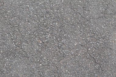 Yıpranmış asfalt, gömülü taşlar ve ince çatlaklarla pürüzlü, granüler bir yüzey gösteriyor..