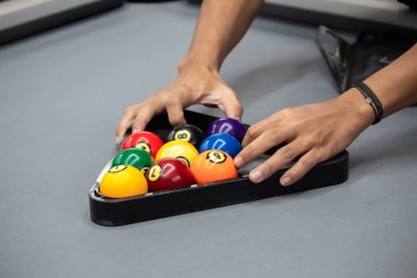 Becerikli eller, gri bir bilardo masasında oynamaya hazır, raflardan oluşan üçgen şeklinde renkli bilardo toplarını düzenler..