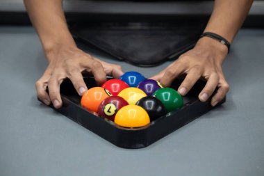 Becerikli eller, gri bir bilardo masasında oynamaya hazır, raflardan oluşan üçgen şeklinde renkli bilardo toplarını düzenler..
