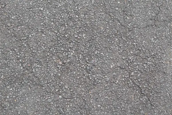 Yıpranmış asfalt, gömülü taşlar ve ince çatlaklarla pürüzlü, granüler bir yüzey gösteriyor..