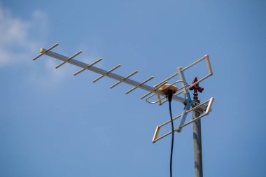 Gümüş TV anteni açık mavi gökyüzüne karşı bir direğe monte edildi. Antenin birden fazla elementi var ve eş eksenli kabloya bağlı..
