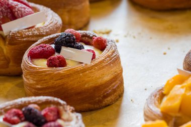 Taze meyve ve kremayla dolu birkaç hamur işi. Hamur işlerinde altın kahverengi bir kabuk var ve üzeri çeşitli böğürtlenler ve dilimlenmiş mangolarla kaplı..