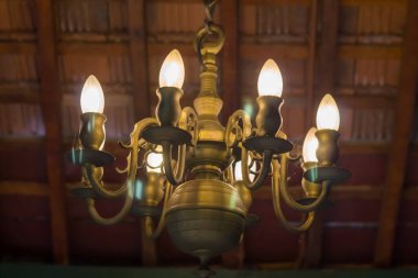 Tarihi bir bina ve klasik bir odada tavandan veya çatıdan sarkan mum ampulleri olan eski moda pirinç avize. Parlak süslemeli, ortaçağ, antik ve antika aydınlatma armatürü bir malikanede.