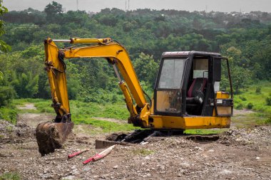 Arka plandaki yeşil dağ vadisinde yeni inşaat alanında büyük bir kazıcı var.