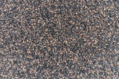 Düzensiz şekilli çakıl ve çakıl taşları koyu ve açık tonlarda kaba, tanecikli bir doku yaratıyor..