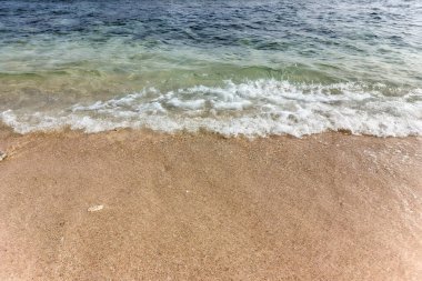 Kum ve su arasında net bir ayrılık olan kumlu bir sahile vuran köpüklü dalgalar..
