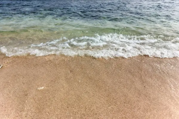 Kum ve su arasında net bir ayrılık olan kumlu bir sahile vuran köpüklü dalgalar..