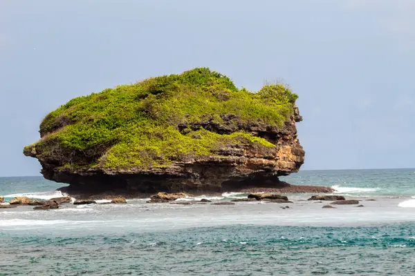Sahil manzarası, kumlu bir sahil, yumuşak dalgalar ve açık mavi gökyüzünün altında birkaç kayalık ada içerir..