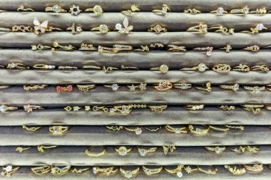 Karmaşık tasarımları ve pırıl pırıl mücevherleri olan sayısız altın yüzüğün yakın plan çekimi, gri, kadife bir mücevher tepsisinde düzgünce sergilenmektedir..