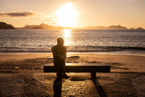 Beautiful sunrise view to poet statue sitting on beach bench in Copacabana, Rio de Janeiro, Brazil