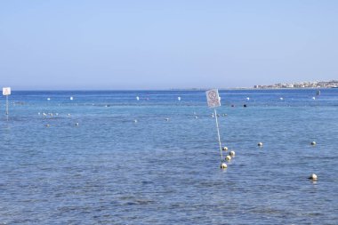 Bu görüntü, yüzen şamandıralar ve suya dağılmış giriş izleriyle denizin huzurlu bir görüntüsünü yakalar. Ufuk berrak bir gökyüzünün altında uzanıyor, huzurlu bir deniz manzarası sağlıyor..