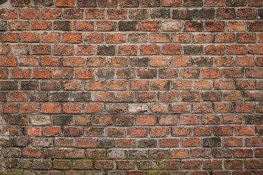 Eski kırmızı tuğlalı bir duvarın detaylı bir görüntüsü zengin dokular, renk değişimleri ve doğal hava şartları sergiliyor. Görüntü pürüzlü yüzeyi ve düzensiz tuğla düzenini vurguluyor.