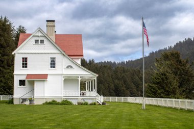 Oregon 'un Pasifik Sahil Otobanı boyunca görkemli bir şekilde tünemiş ikonik bir deniz feneri ve tarihi bekçisinin evi manzaranın simgesi olarak duruyor. Engebeli sahil kayalıkları arasında panoramik okyanus manzaraları sunuyor..