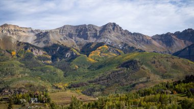 Telluride, Colorado 'nun dışındaki San Juan Dağları' nın geniş bir manzarasında altın kavak ağacı çizgileri engebeli tepeler ve yumuşak bir gökyüzünün altındaki gür orman yamaçlarında parlak bir sonbahar deseni çiziyor..