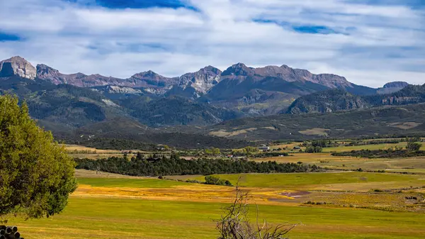 Uçsuz bucaksız bir çayır dramatik Colorado sıradağlarının altında, yumuşak mavi bir gökyüzünün altında yükselen katmanlı tepeler ve engebeli tepelerle altın renklere bürünür. Bu canlı manzara, sonbahara geçiş dönemini ve Rocky Dağları 'nın görkemli güzelliğini yansıtıyor..
