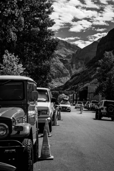 Telluride, Colorado 'da klasik bir Toyota Land Cruiser' ın büyüleyici bir dağ caddesinde park ettiği nostaljik bir siyah-beyaz sokak sahnesi. Arkaplanda yüksek kayalık kayalıklar, çizgi araçlar ve dramatik bulutlar yer alıyor..