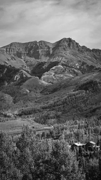 Telluride yüksek kesiminin geniş siyah-beyaz manzarası katmanlı tepeleri ve ormanlık yamaçları dramatik, pürüzlü tepelere doğru tırmanırken yakalıyor. Vadideki sakin bir yerleşim bölgesi, vahşi araziye insan ölçeği ekliyor..