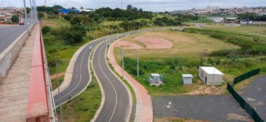 Yeşil alanlar ve bitki örtüsüyle çevrili, dolambaçlı bir yol manzarası. Görüntü bulutlu bir gökyüzüne sahip, bir sükunet ve doğa ile bağlantı hissi uyandırıyor..