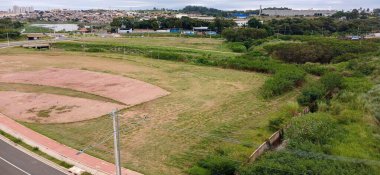 Düşük bitki örtüsüyle işaretlenmiş ve kentsel bir manzarayla çevrili boş bir arazinin panoramik görüntüsü. Arka planda, binaları ve kentsel altyapısı olan şehir. Görüntü, sakinliği ve doğa ile kentsel etkileşimi iletir.