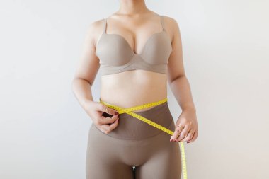 Bel çevresindeki ölçü bandını kullanan, spor, sağlık ve vücut hedeflerine odaklanan kadın..