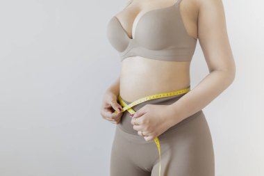 Kıvrımlı kadın, bel ölçüsünü spor kıyafetiyle sarı bantla alıyor, sağlığı ve şekli takip ediyor..