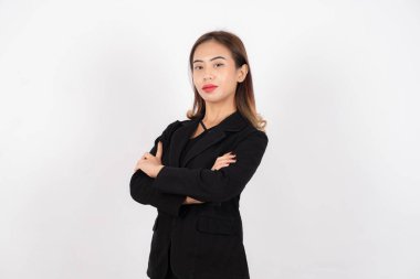 Siyah takım elbiseli genç profesyonel bir kadın beyaz arka planda kollarını kavuşturup poz veriyor..
