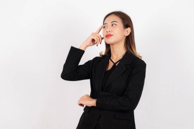 Siyah takım elbiseli profesyonel bir kadın parmağıyla şakağına dokunuyor. Düşünüyor gibi, beyaz tenli..