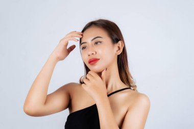 Siyah elbiseli genç bir kadın düşünceli bir ifadeyle poz veriyor ve elleri çenesinde, açık arkaplanda..