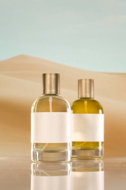 Boş beyaz etiketli iki minimalist parfüm şişesi, temiz, doğal bir estetik yansıtan ve zarafet ve basitlik temaları anımsatan yumuşak bir çöl zeminine karşı duruyor..