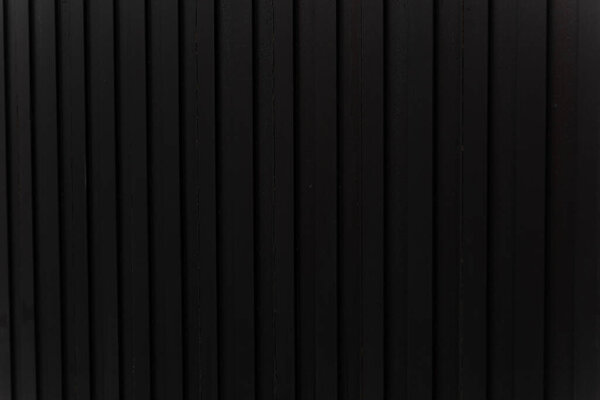 Close-up of a vertical black slatted wall with evenly spaced lines, showcasing modern industrial design and minimalistic architectural texture.