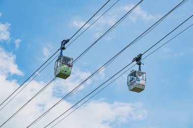 İki renkli gondol, mavi gökyüzünde bir teleferiğe biner.
