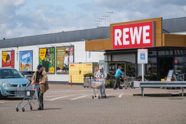 REWE süpermarket girişinde arabaları olan insanlar.