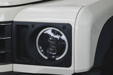 Şehrin caddesinde park etmiş beyaz bir INEOS Grenadier SUV 'un farına yakın çekim.