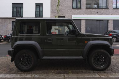 Koyu yeşil arazi aracı Suzuki Jimny sakin bir şehir sokağına park etmiş.