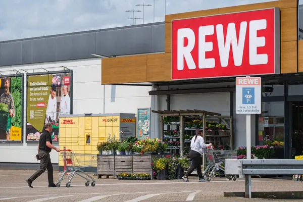 REWE süpermarket girişinde arabaları olan insanlar.