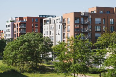 Güneşli kentsel bir mahallede ağaçları olan modern apartmanlar.