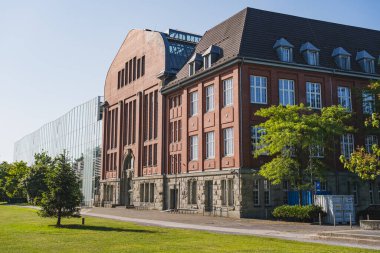 Modern cam uzantısının yanındaki kırmızı tuğlalı tarihi bina.