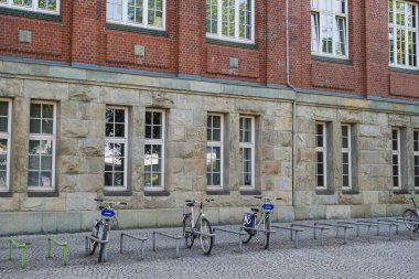 Taş ve tuğla bir üniversite binasının önüne park edilmiş bisikletler.