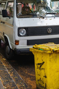Eski Volkswagen minibüs ve düşmüş ağaç artıklarıyla kaplı sarı çöp tenekesi.