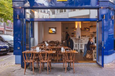 Açık kapıları, ahşap sandalyeleri ve içinde bir barı olan rahat bir sokak kafesi.