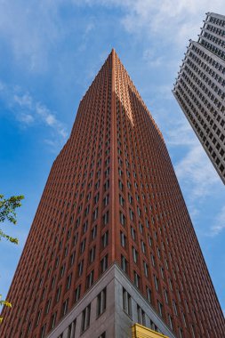 Uzun kırmızı tuğlalı gökdelen parlak mavi gökyüzüne doğru hızla yükseliyor.