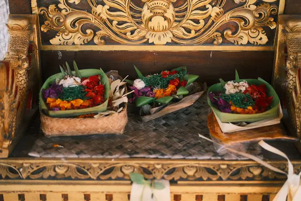 Canlı renkli çiçekler ve yeşil yapraklarla dolu üç adet titizlikle hazırlanmış Balili Kanang Sari sunağı güzel oyulmuş altın bir sunağa konur.