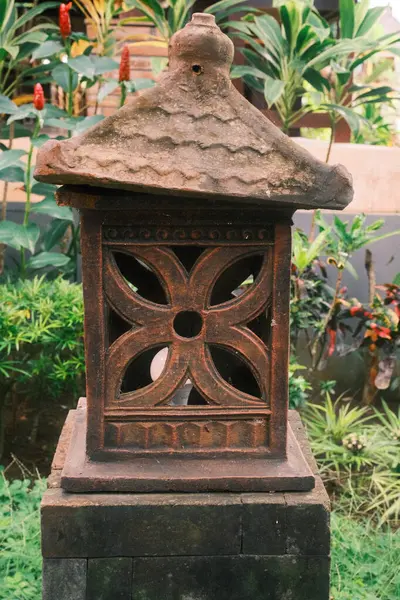 Zamanla yıpranmış geleneksel bir Bali taş bahçe feneri detaylarıyla ve verimli bir bahçe düzeninde pagoda tarzı çatısıyla gururla durur.