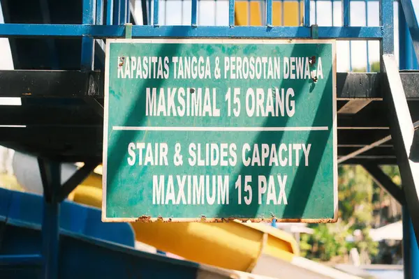 İki dilli işaret, merdivenlerin maksimum kapasitesi için açık talimatlar verir ve bir su parkında kayar