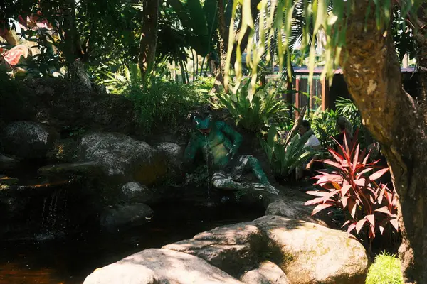 Kemenuh, Bali - 27 Nisan 2025: Heykel stratejik olarak doğal kayalar ve canlı yeşil bitkilerin arasına yerleştiriliyor, bahçenin sakin ve mistik bir köşesini oluşturuyor.